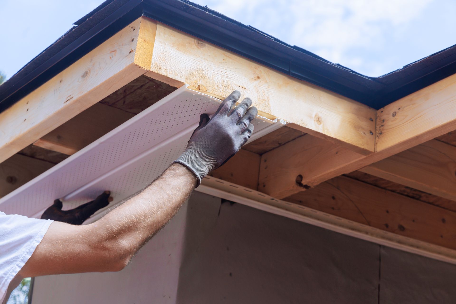 Person installing white perforated soffit panel on a building’s overhang.