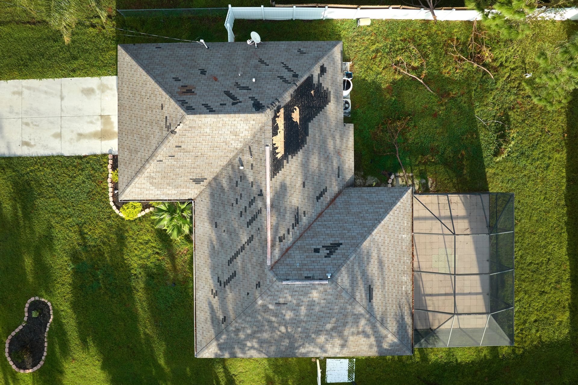 Aerial view of a residential house with a dark shingled roof, surrounded by green grass and a backyard screen enclosure.
