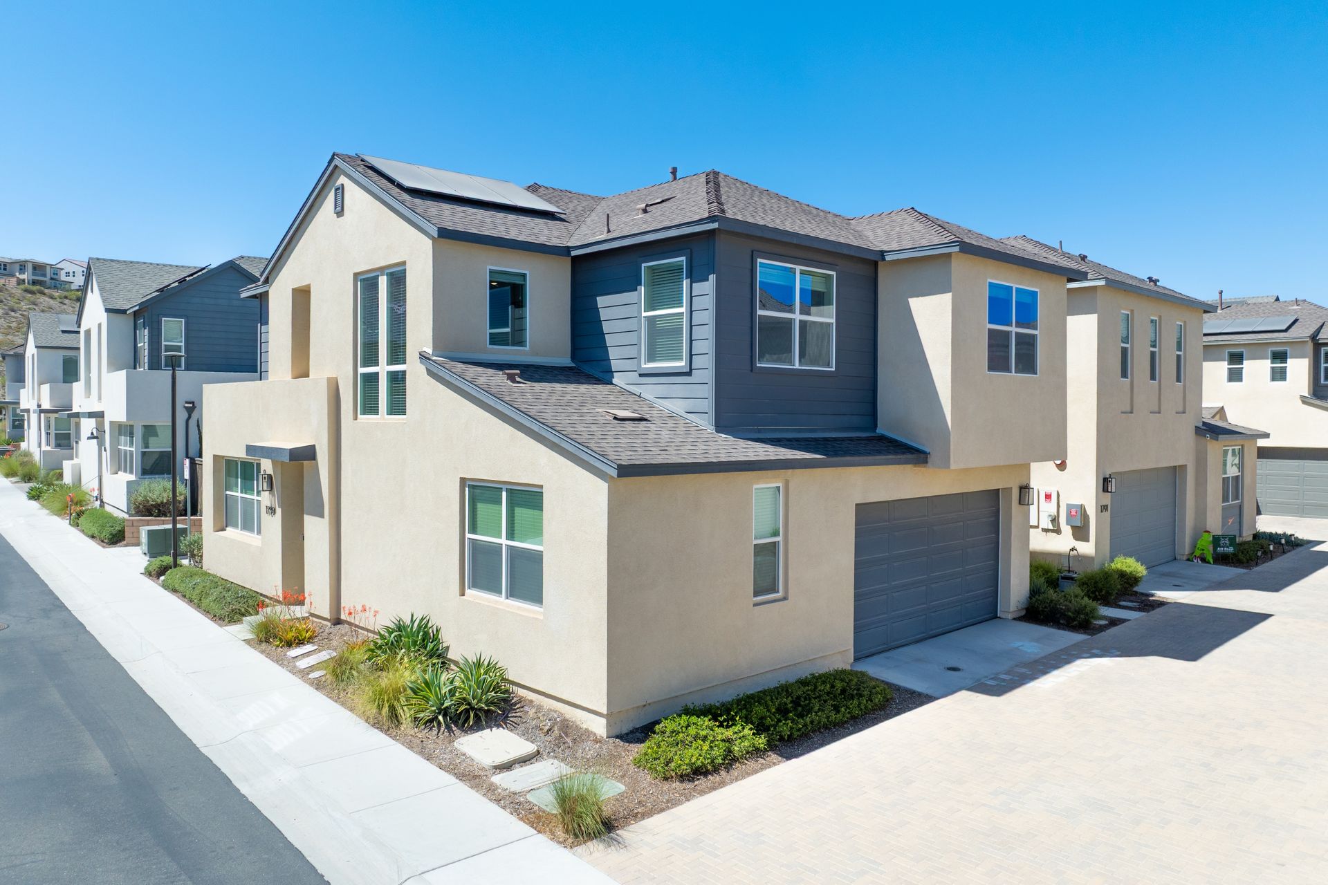 A modern multi-story townhouse complex with beige and dark gray siding under a clear blue sky.
