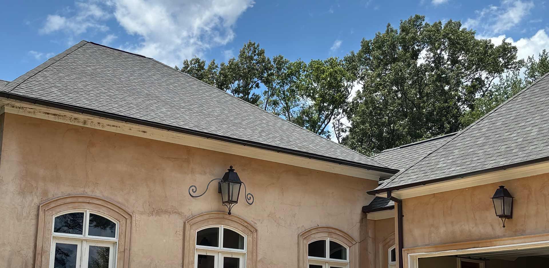 Exterior view of a stucco house with arched windows and a dark gray tiled roof against a blue sky.