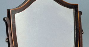 A dark-framed, shield-shaped vanity mirror on a light background.