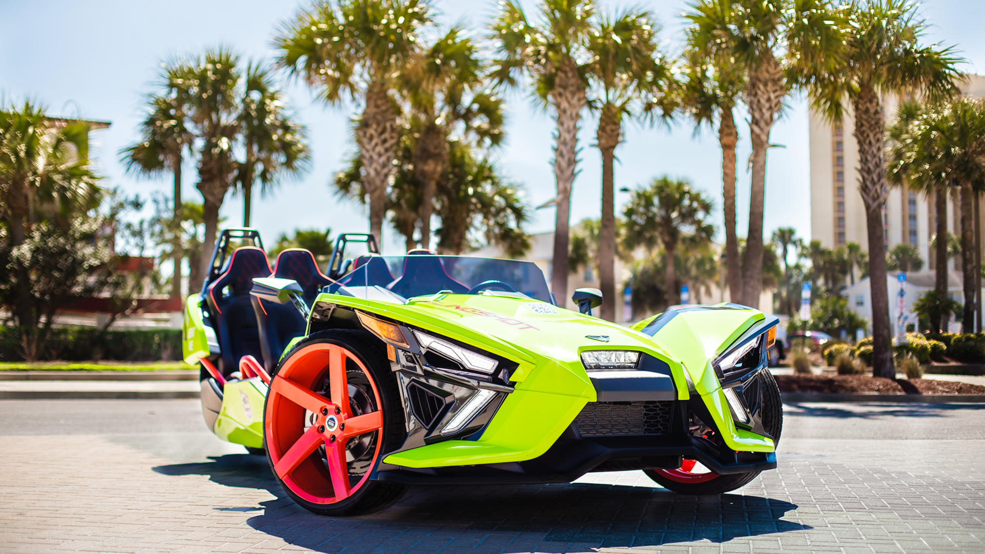 A green slingshot is parked on the side of the road in front of palm trees.