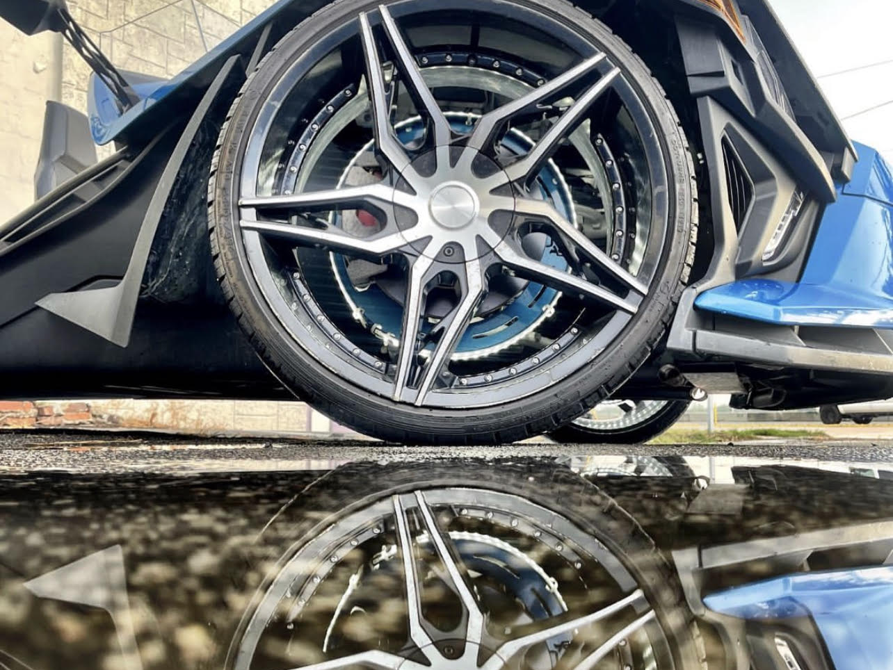A close up of a car wheel with a reflection in the water.