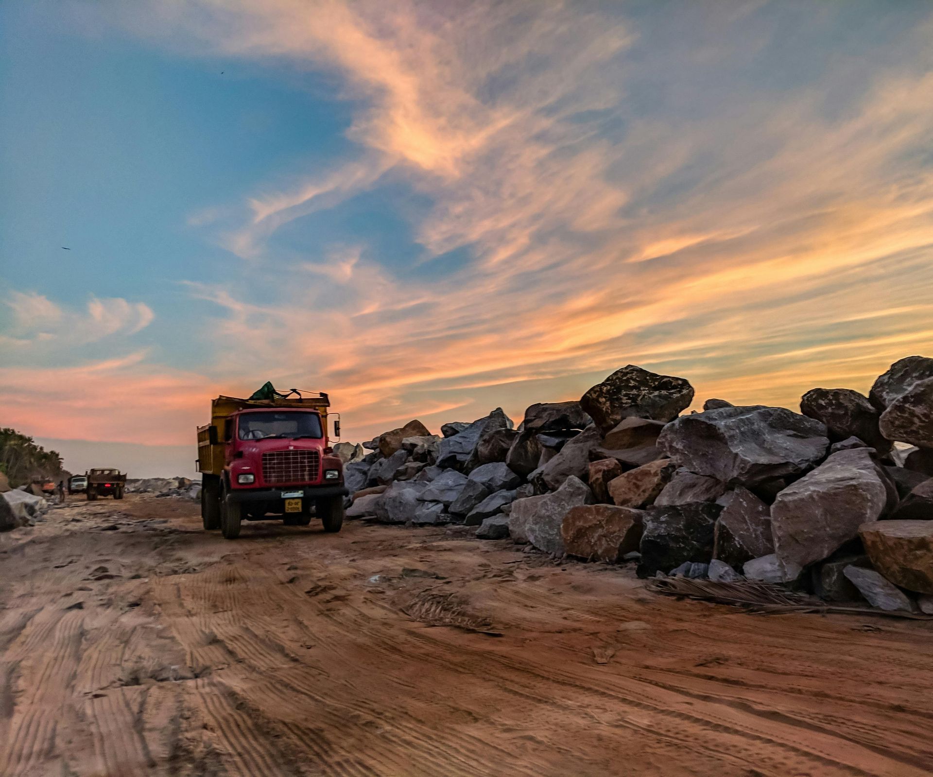 A red truck is driving down a dirt road next to a pile of rocks.