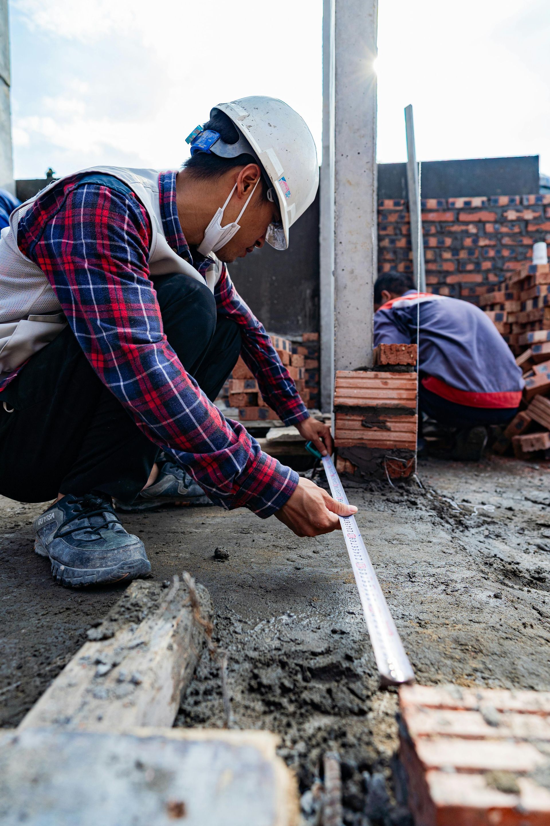 A construction worker is measuring a brick wall with a tape measure.