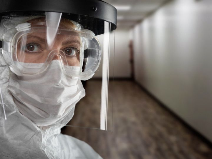 a woman wearing a mask , goggles and a face shield is standing in a hallway