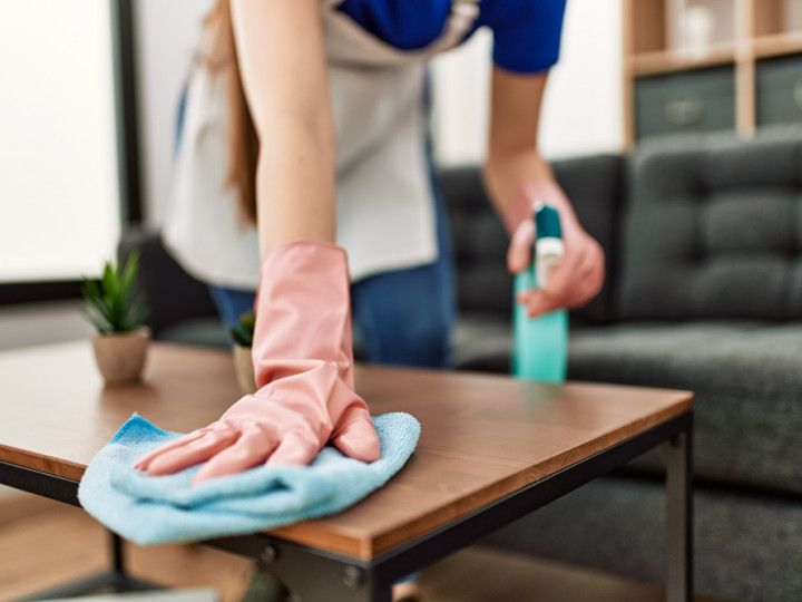 a woman wearing pink gloves is cleaning a wooden table in a living room