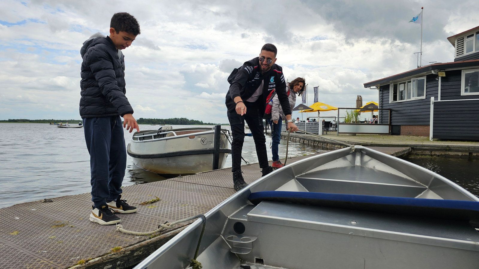 שלושה אנשים ליד סירה על מזח. אחד מצביע לכיוון הסירה, ביום מעונן.