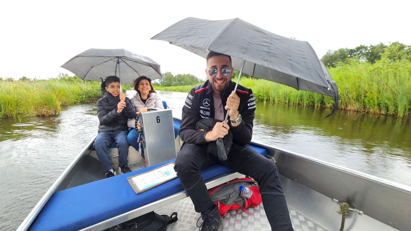 שלושה אנשים בסירה תחת שמשיות ביום גשום. גבר בחזית מחייך.