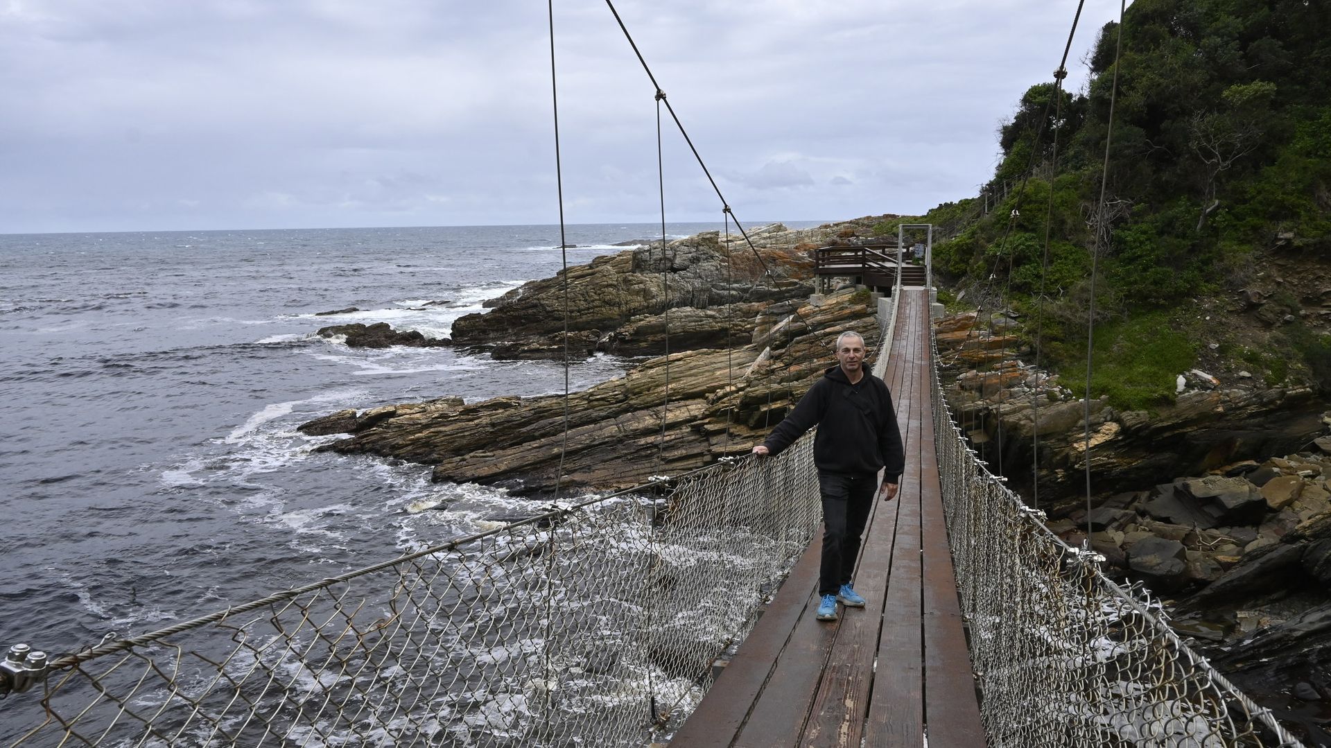 אדם צועד על פני גשר חבלים מעל גוף מים