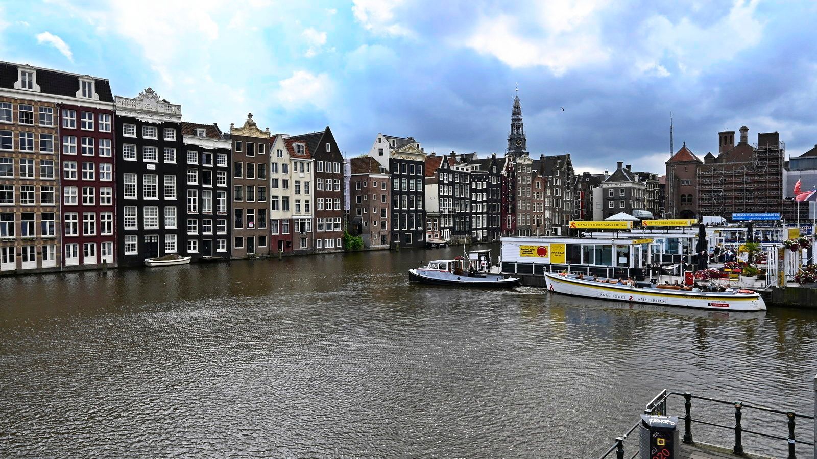 תעלה באמסטרדם עם בניינים צבעוניים, סירות ושמיים מעוננים.