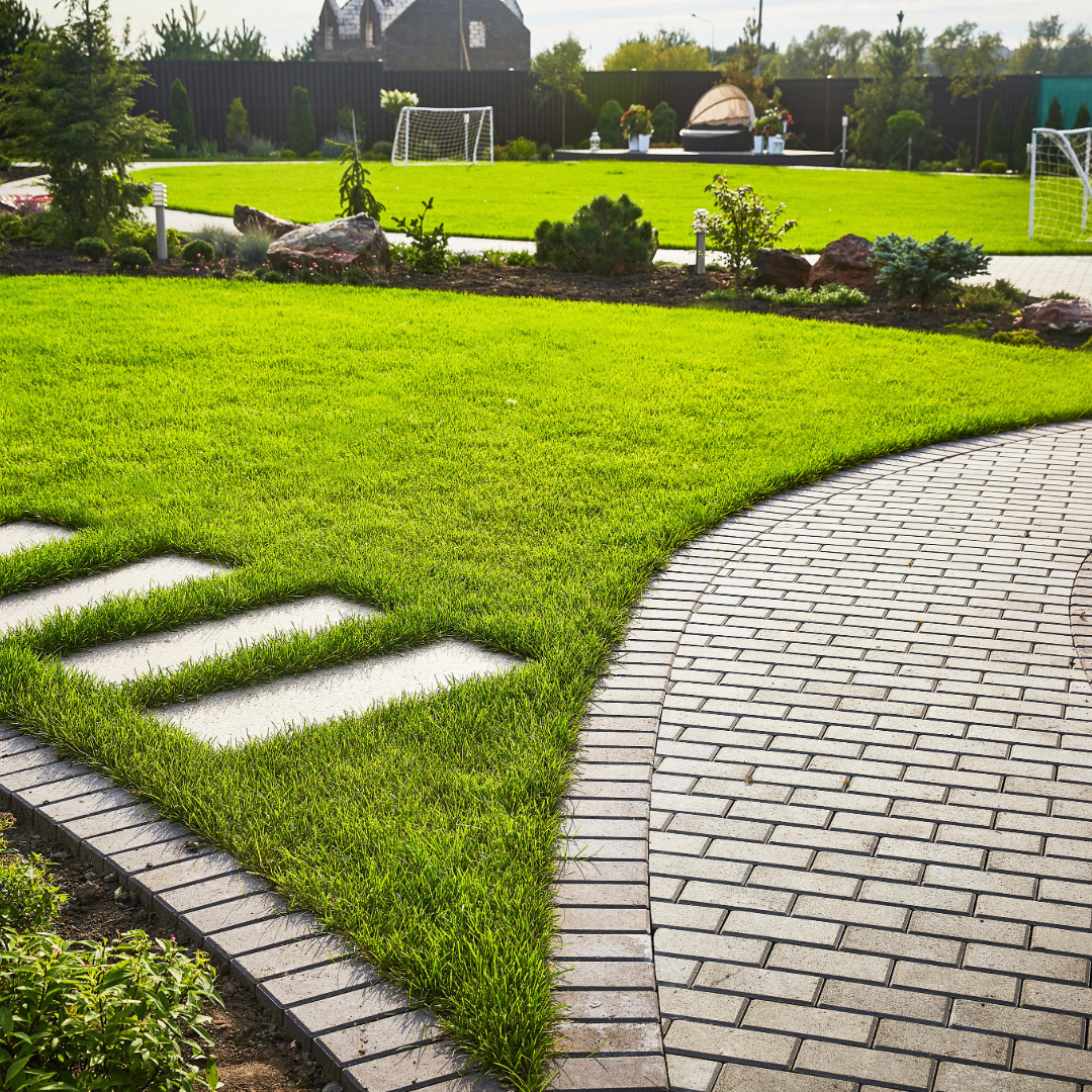 A brick walkway leading to a large lush green field.