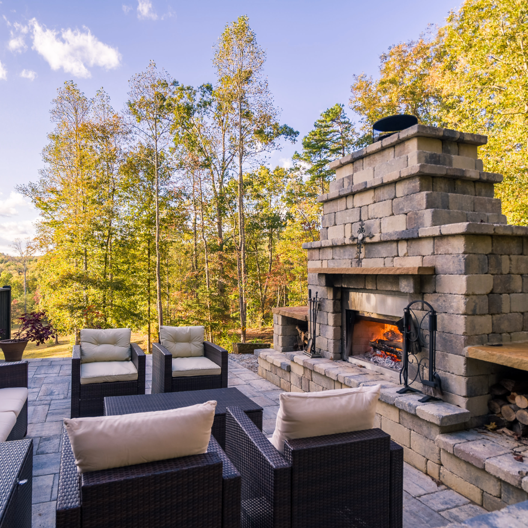 A patio with chairs and a fireplace with trees in the background