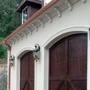 A garage with two wooden garage doors and a copper gutter.
