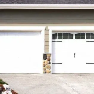 A house with two white garage doors and a stone pillar.