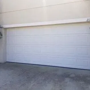 A white garage door is open on the side of a house.