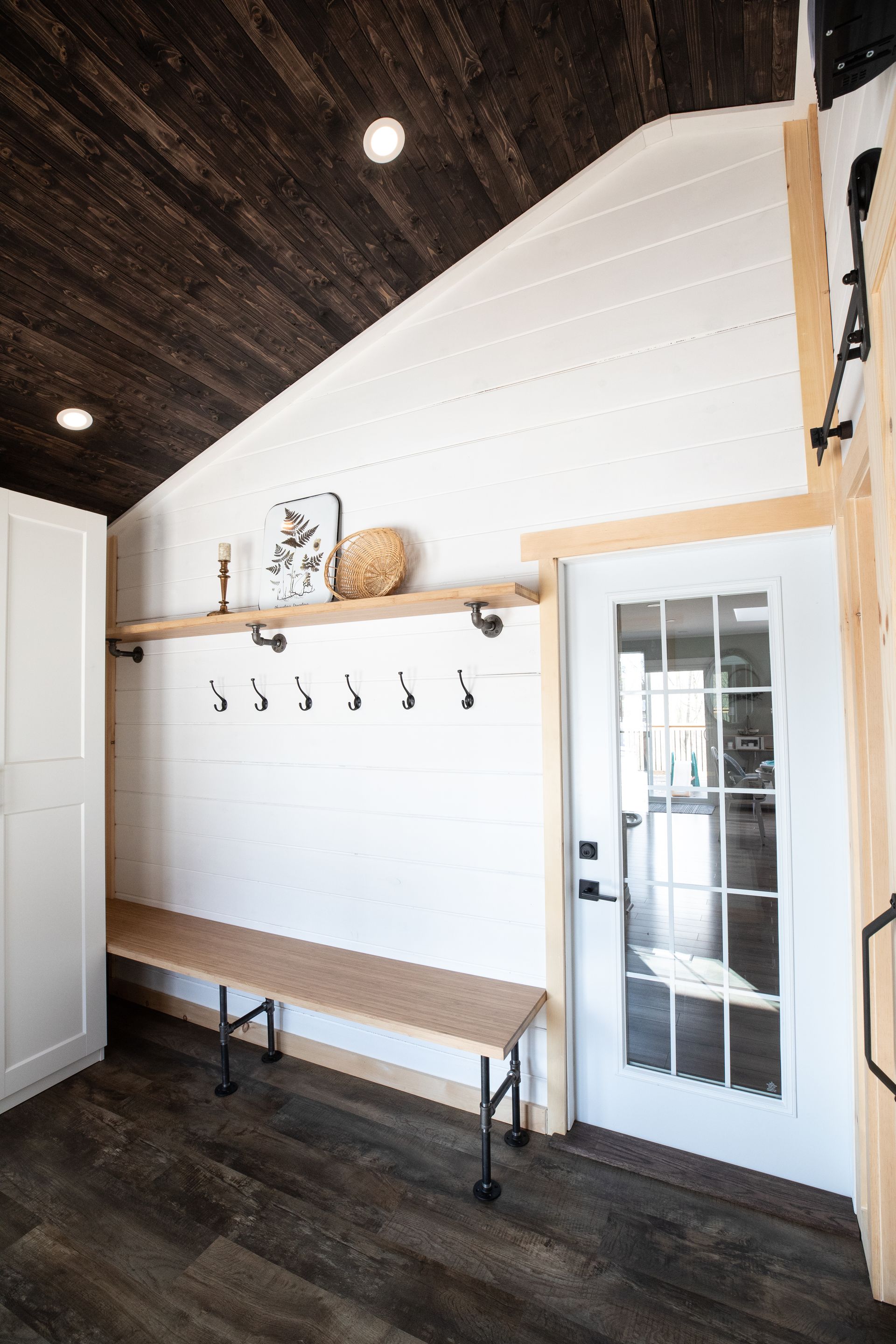 Entryway with white storage cabinets, wooden bench, and coat hooks, leading to a glass-paned door.