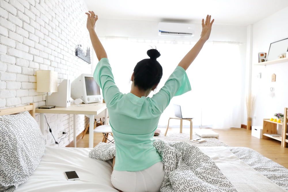 A Woman Is Sitting on A Bed with Her Arms Outstretched — Danzair Refrigeration & Airconditioning in Alstonville, NSW
