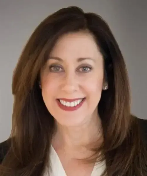 Smiling woman with dark hair in a professional setting, wearing a black blazer over a white top.