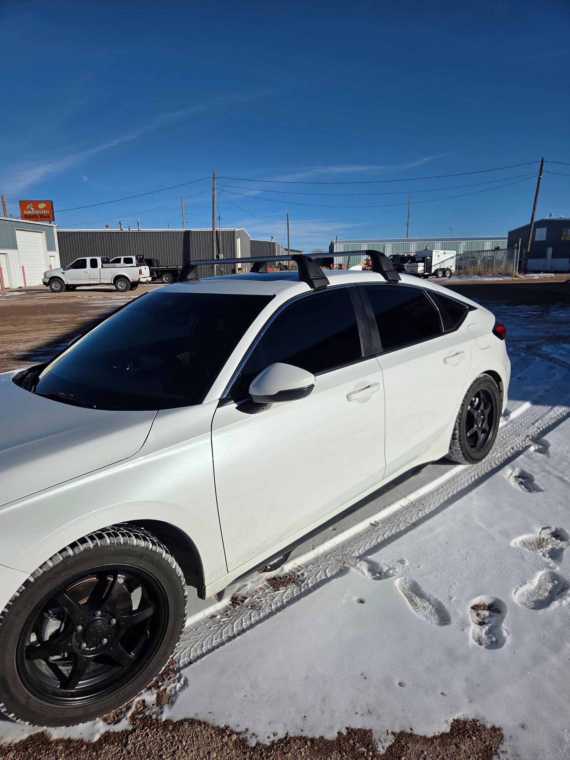 White car with black wheels and roof rack parked on snow, sunny day.