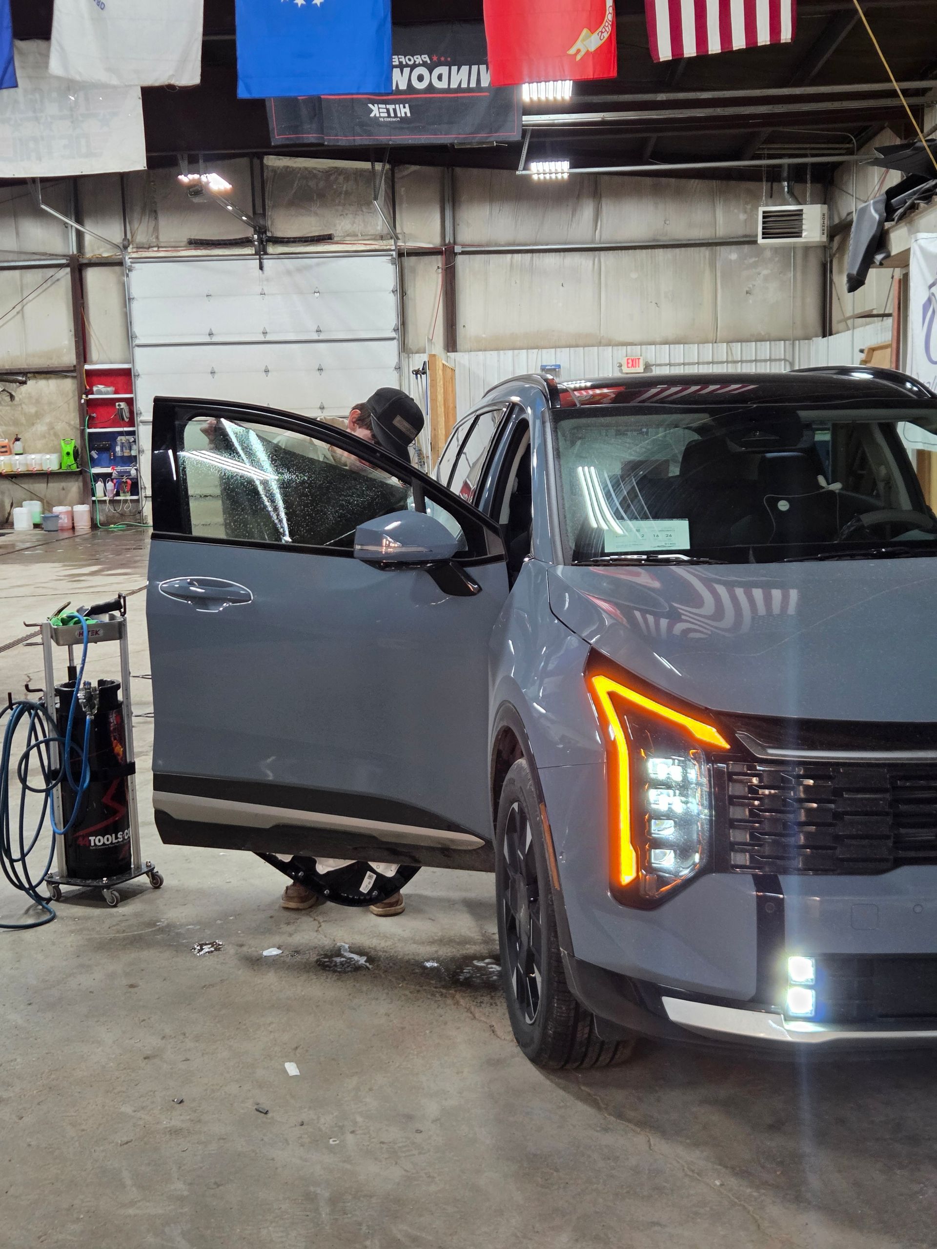 Gray SUV with door open, person inside. Automotive shop setting.