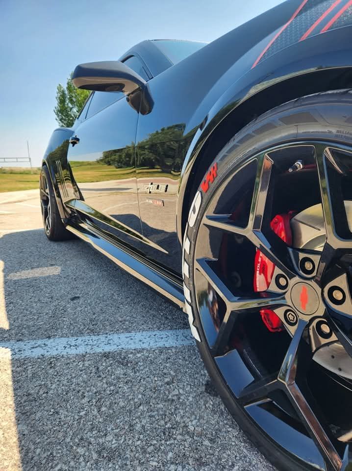 Black sports car with red brake calipers and custom rims parked on asphalt.