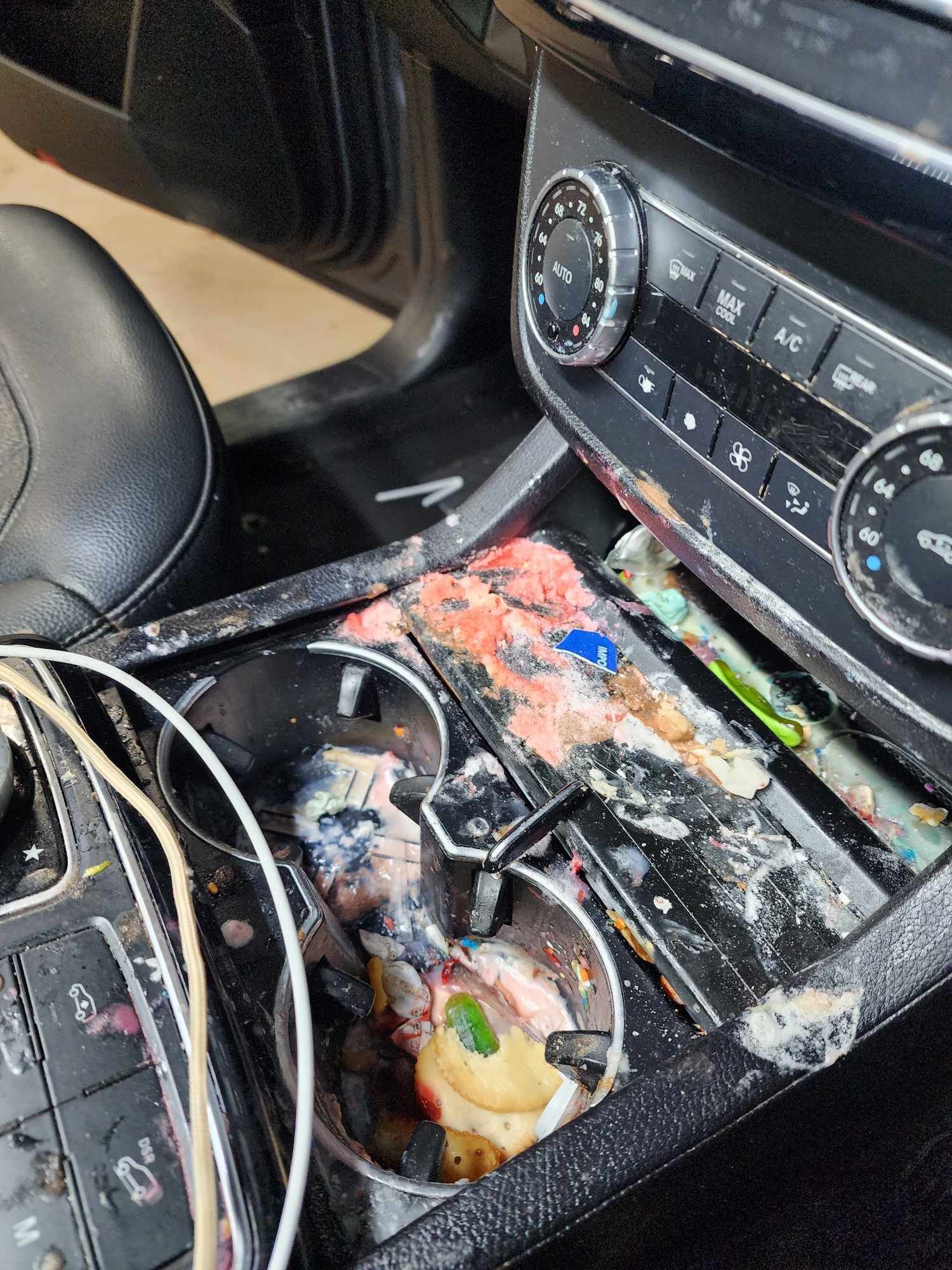 Car's center console with spilled, colorful substances in cup holders and surrounding area, appearing messy.