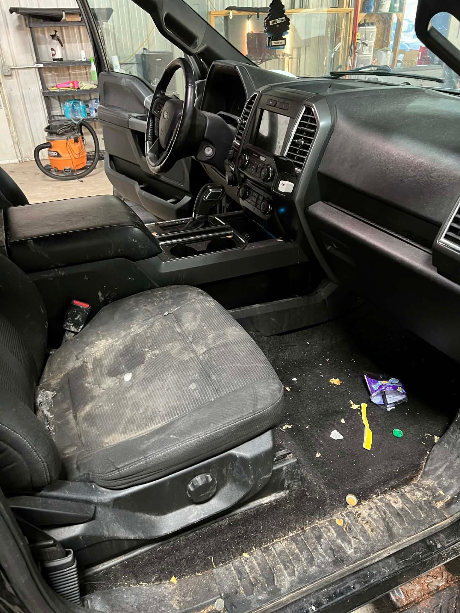 Dirty truck interior with debris on seat and floor, steering wheel, and console.