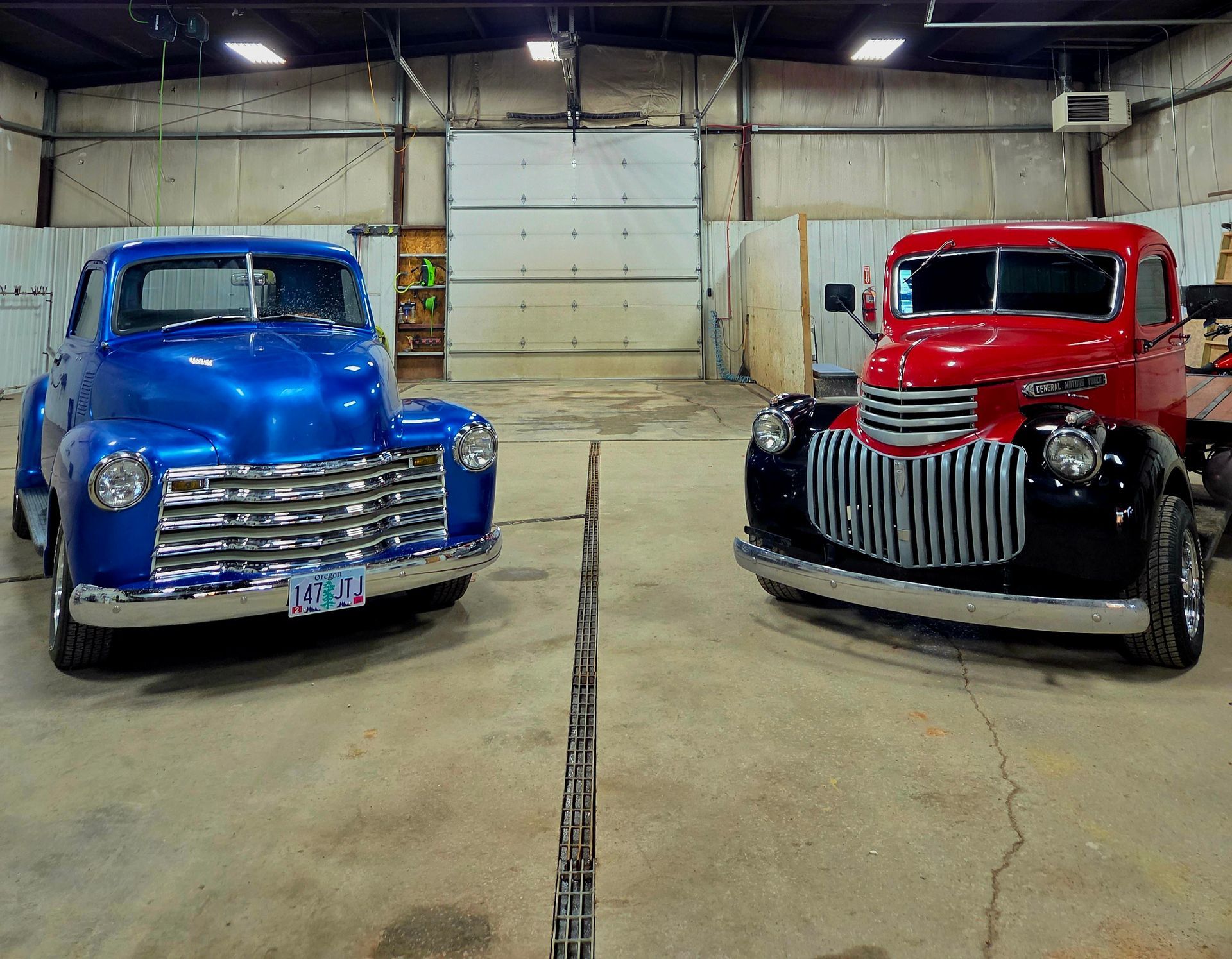 Two classic trucks, one blue and one red, parked inside a garage.