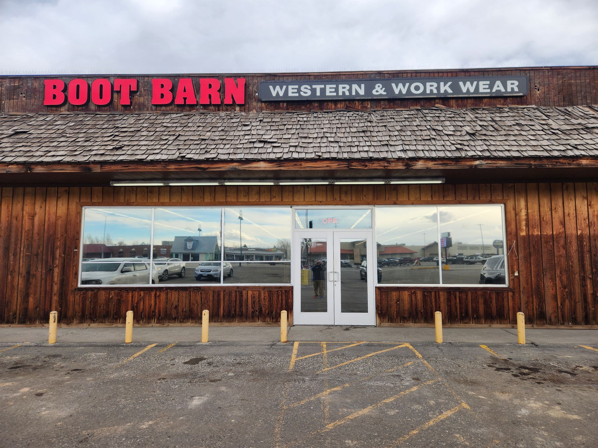 Boot Barn store front with mirrored windows and brown exterior; gray sky overhead.