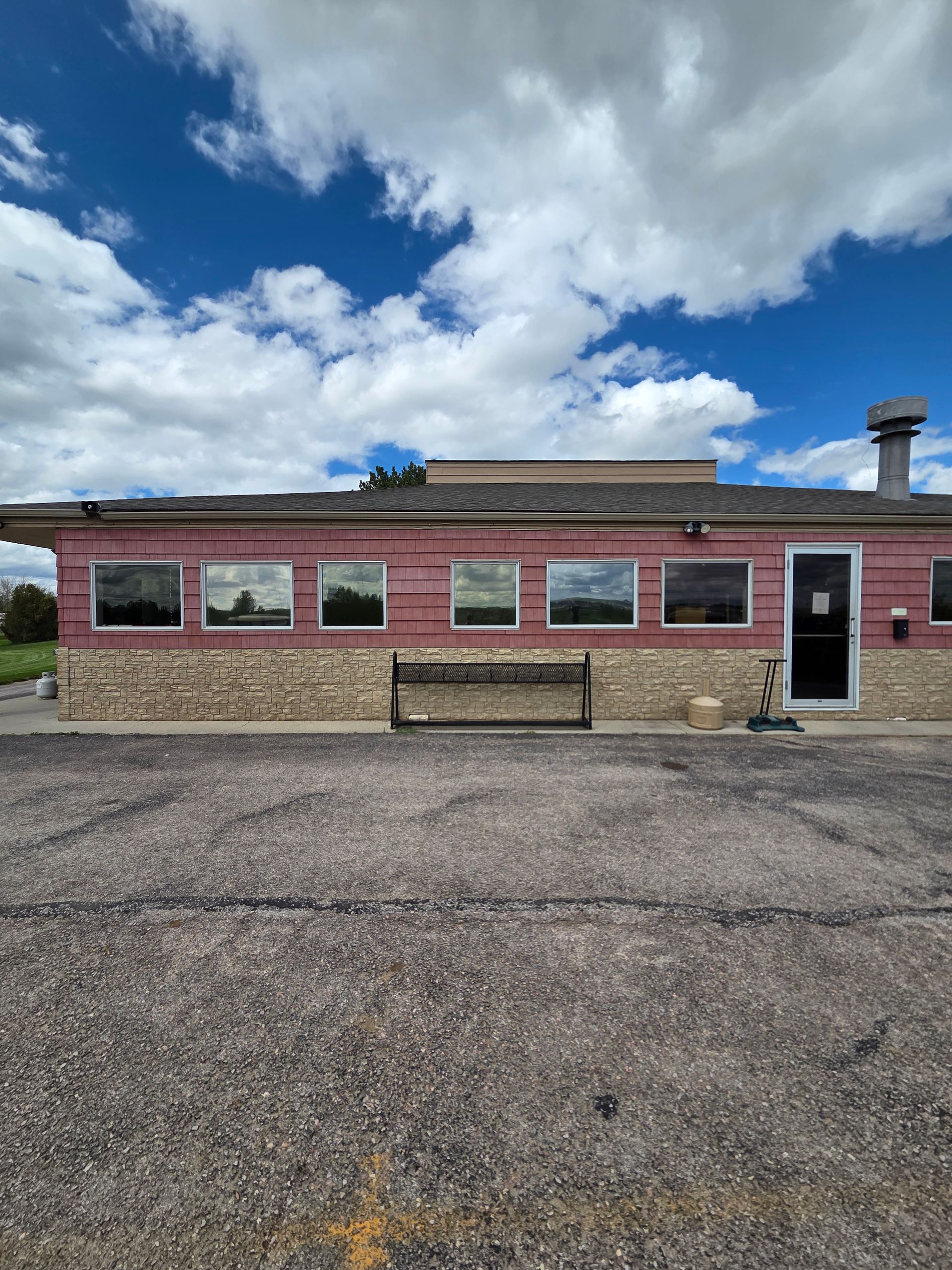 Diner building with pink top, tan stone facade, windows reflecting a landscape, black door, and gravel parking lot.