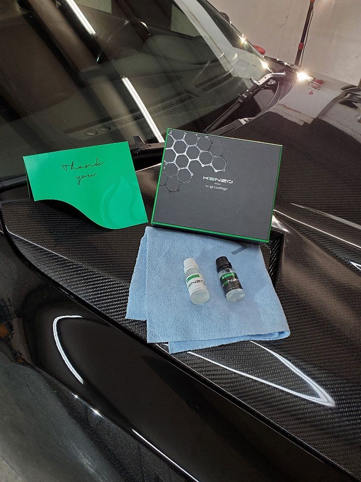 Car detailing kit on a black carbon fiber hood, with box, bottles, a microfiber cloth, and green applicator pad.