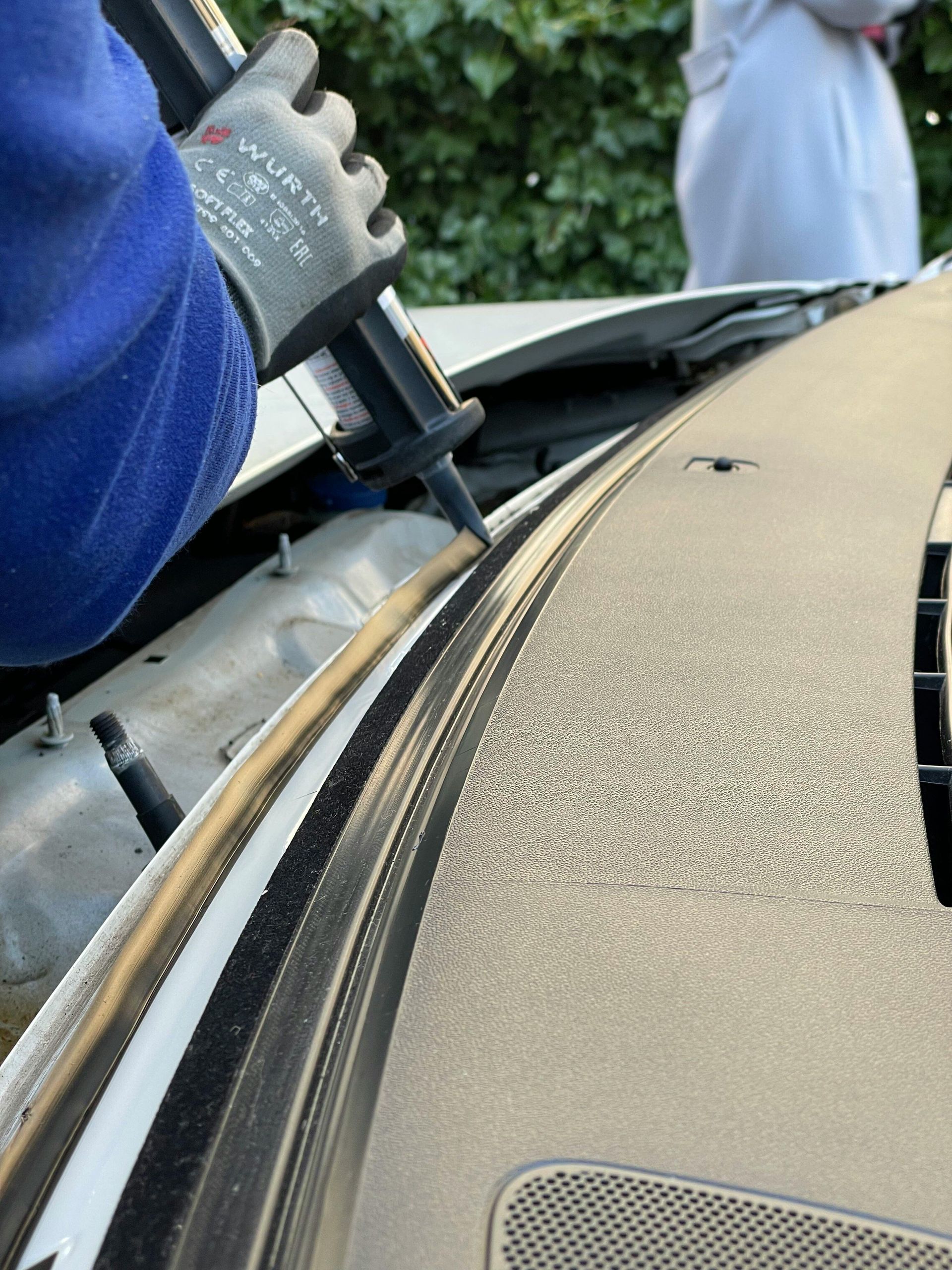 Person applying sealant to a car's dashboard near the windshield, using a black applicator, wearing a glove.