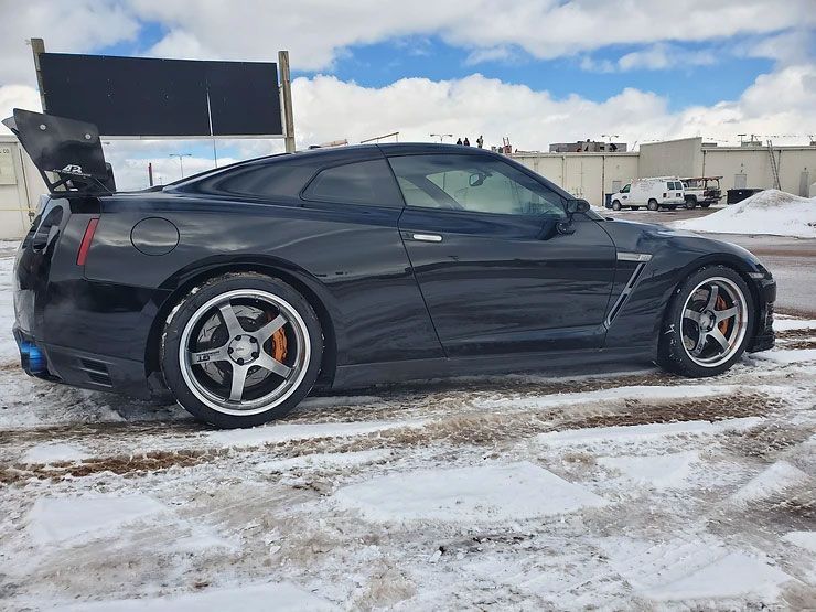 Black Nissan GT-R sports car with open wing spoiler in snowy parking lot.