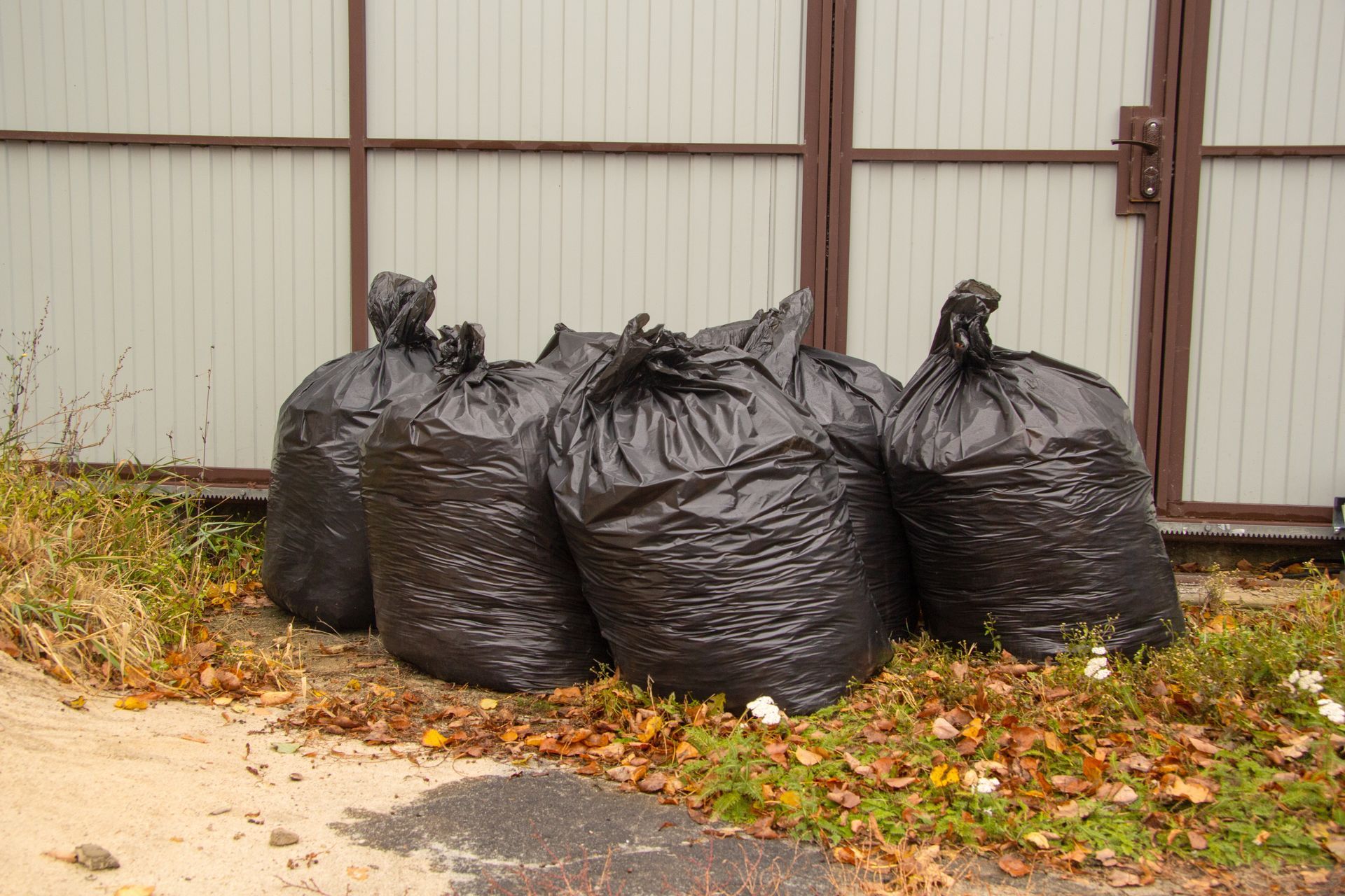 a bunch of black garbage bags are sitting on the ground in front of a fence .