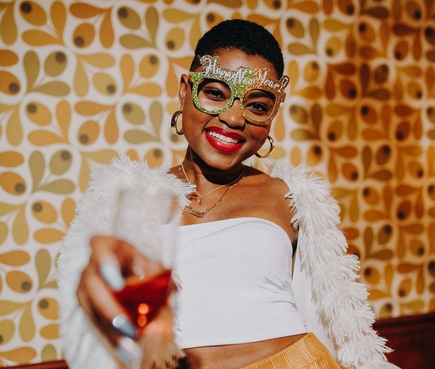 A woman wearing a mask and glasses is holding a glass of wine