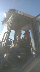 A person and a child sit in the cab of a 416B Caterpillar backhoe loader under a clear blue sky.