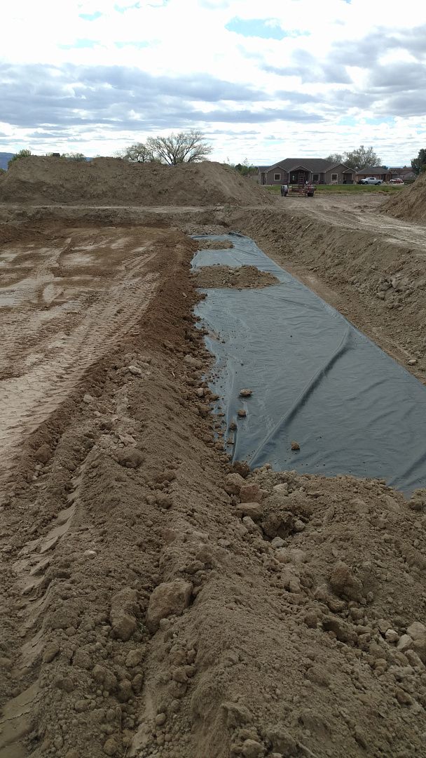 A trench in a dirt construction site partially lined with a black protective fabric.