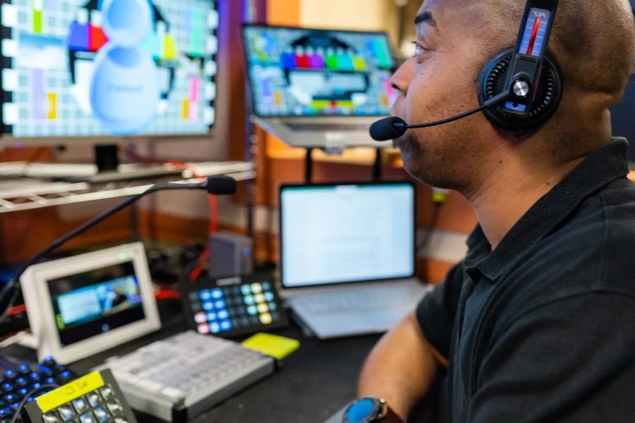 A man wearing headphones and a microphone is sitting in front of a computer.
