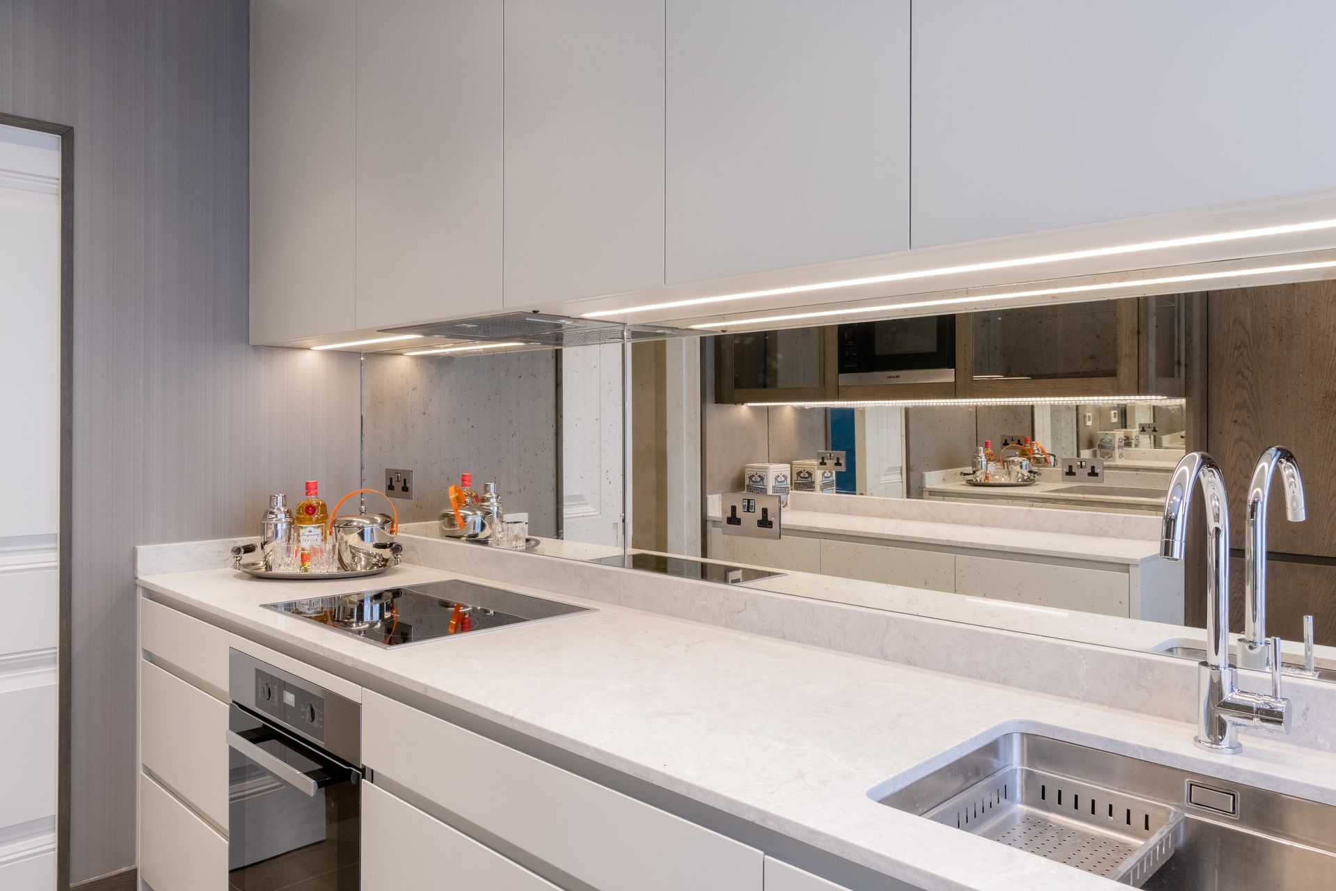 a kitchen with white cabinets , stainless steel appliances , a sink and large mirror