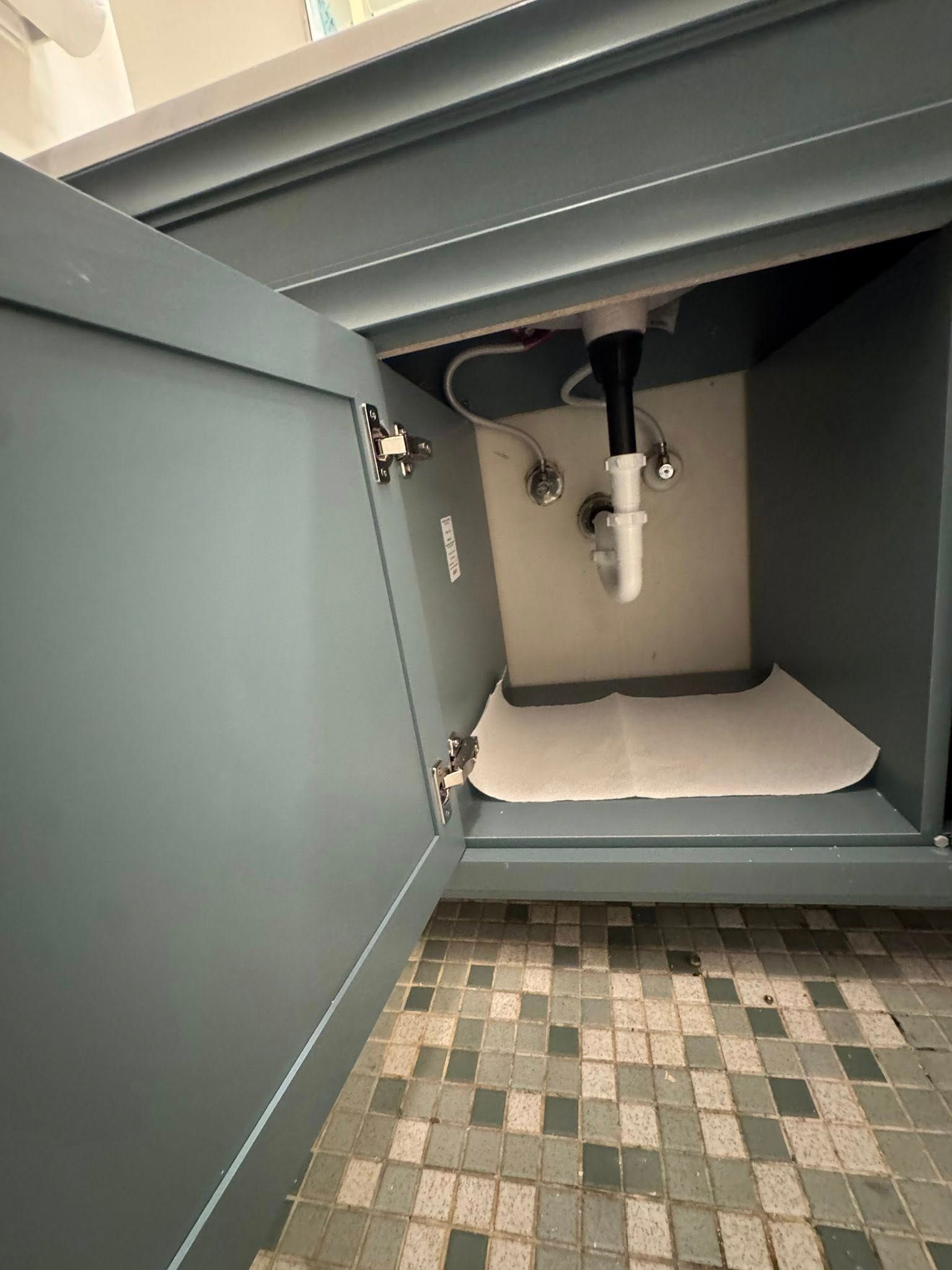 A bathroom sink with the door open and a paper towel underneath it.
