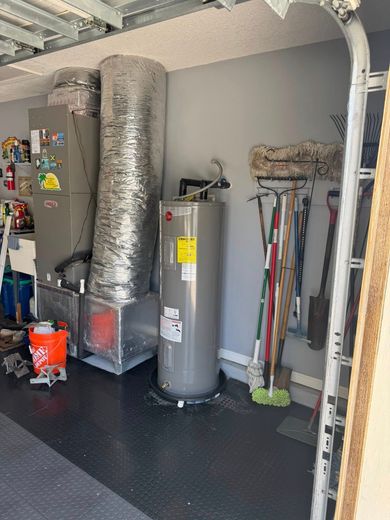 A water heater is sitting in a garage next to a refrigerator.