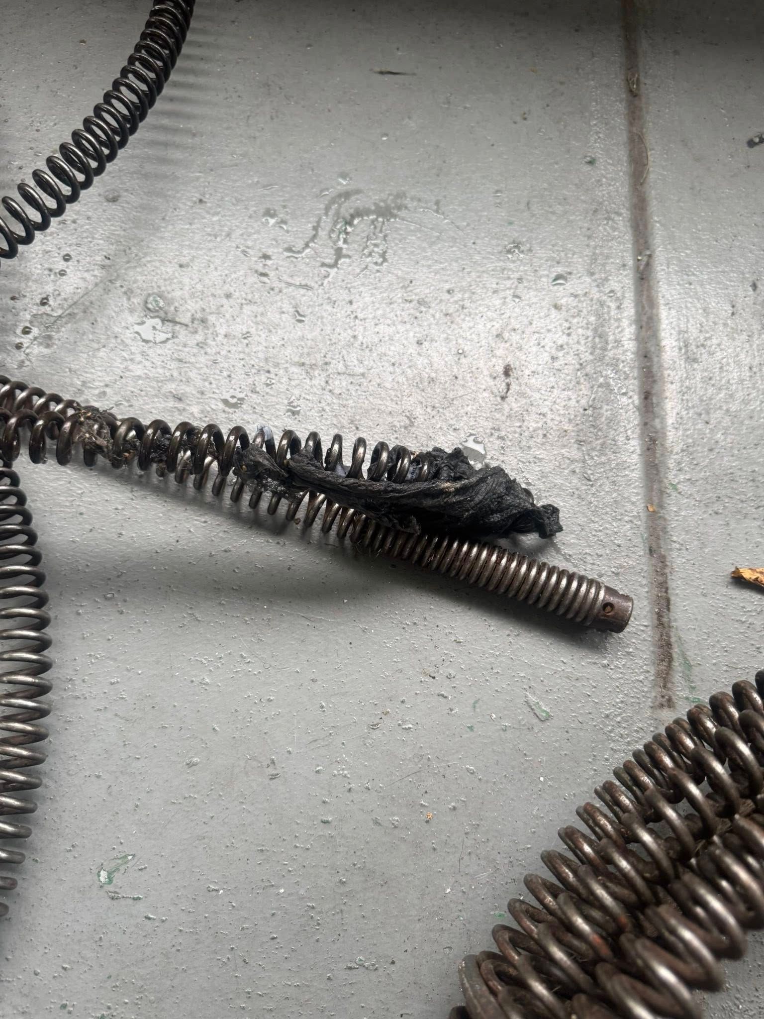 A close up of a drain snake on a tiled floor.