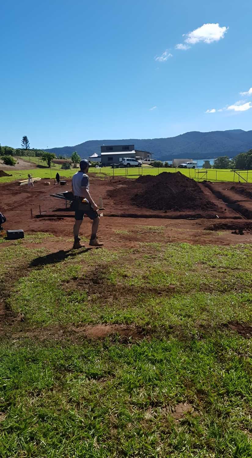 A Man is Standing in a Grassy Field Next to a Pile of Dirt — ROGA Build Solutions in Atherton, QLD