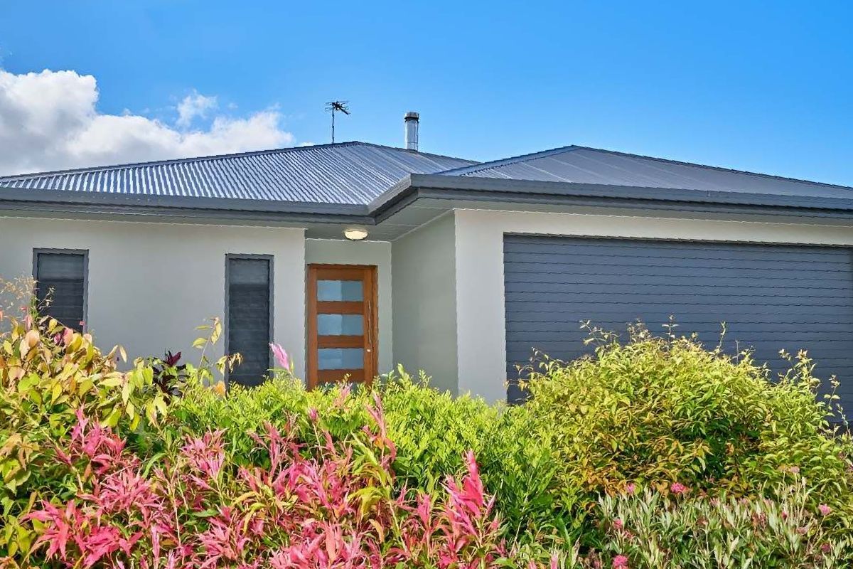 A White House With a Gray Garage Door is Surrounded by Flowers and Bushes — ROGA Build Solutions in Atherton, QLD