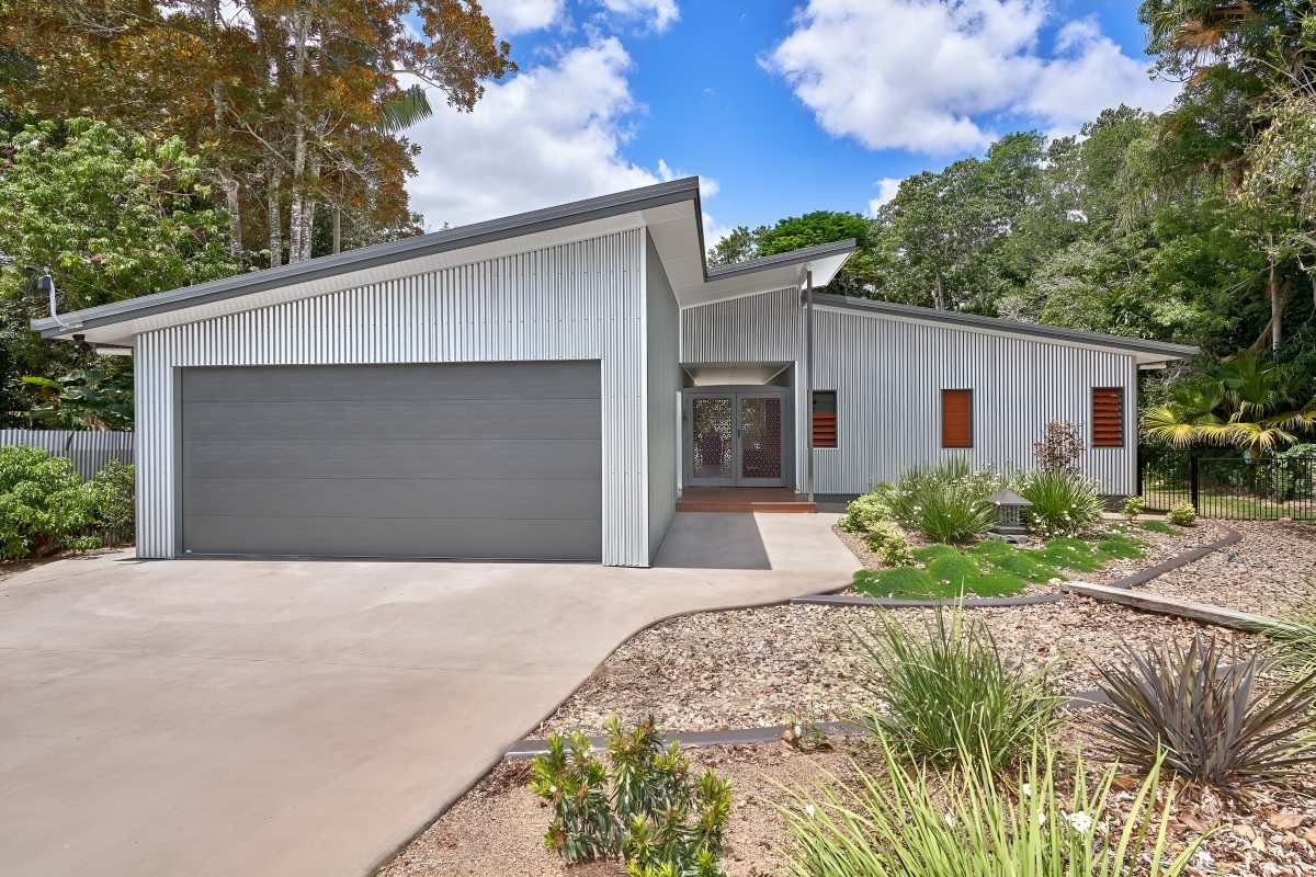 A White House With a Gray Garage Door is Surrounded by Trees — ROGA Build Solutions in Atherton, QLD