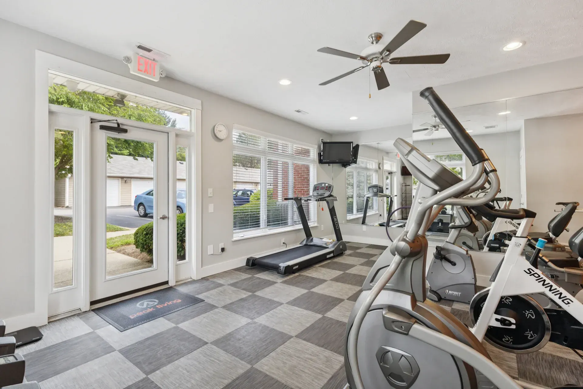 Gym interior with exercise equipment and door to the outside. Gray and checkered floor.