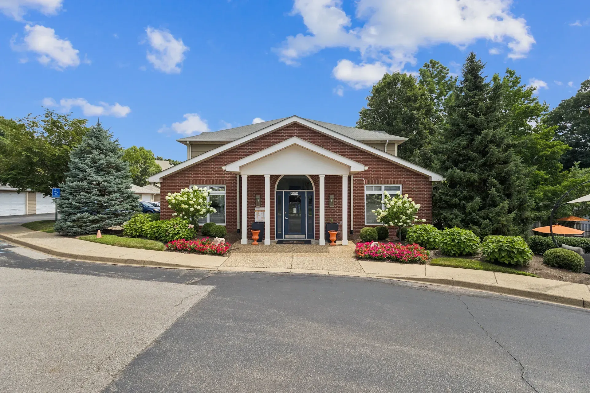 A low-slung brick building with a dark front door, flanked by windows and landscaping under a blue sky.