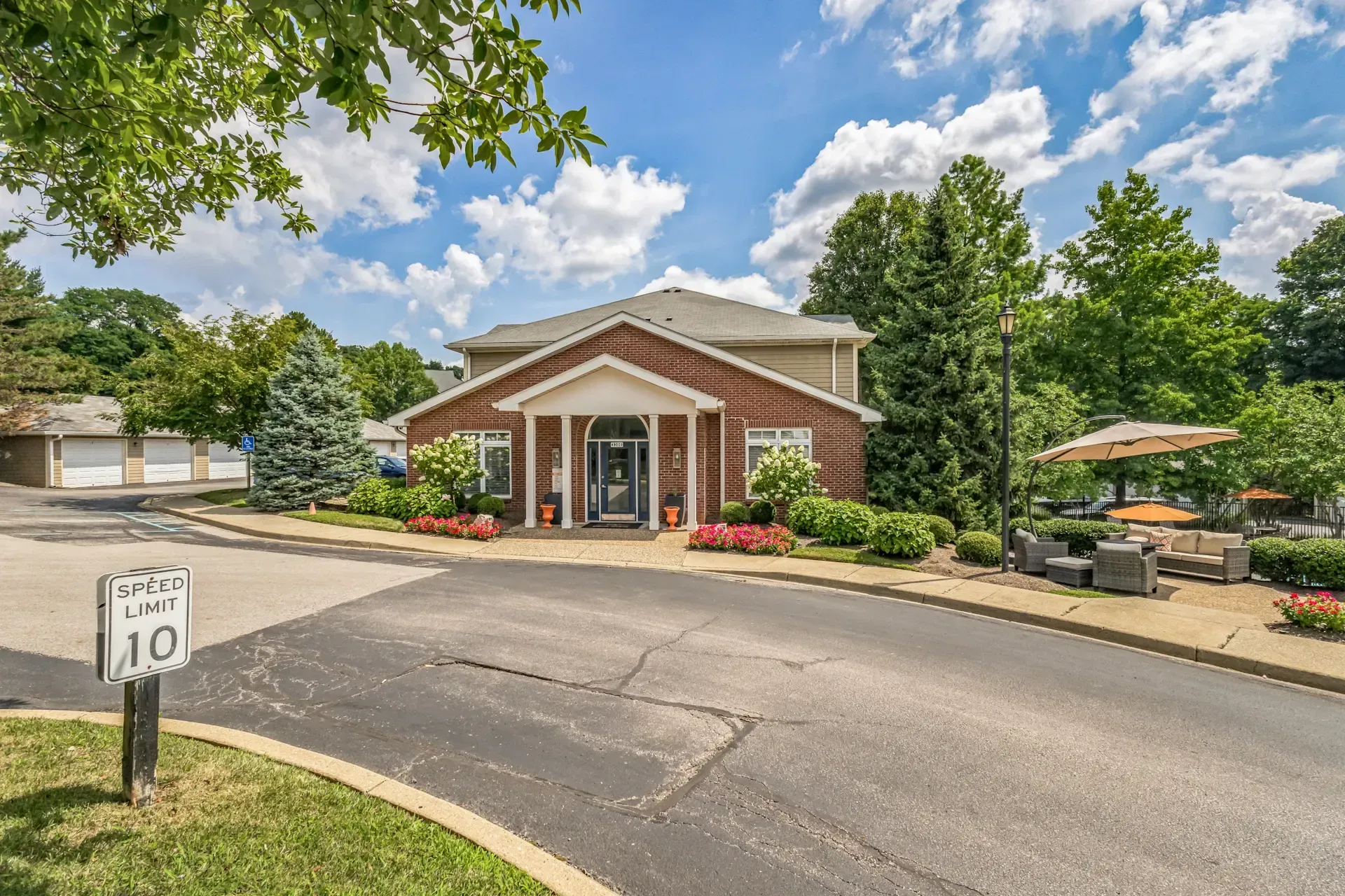 Building with brown and beige facade, entrance with columns, surrounded by trees and landscaping.