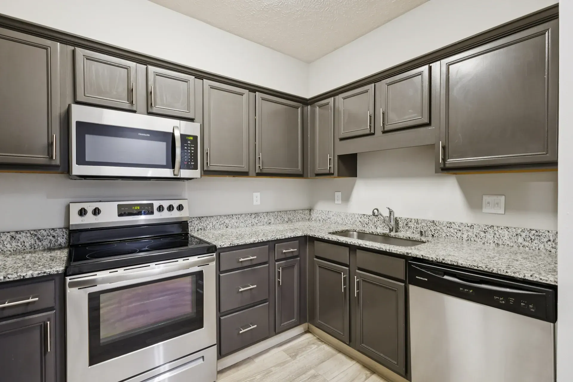 Gray kitchen cabinets, stainless steel appliances, granite countertops, and light flooring.
